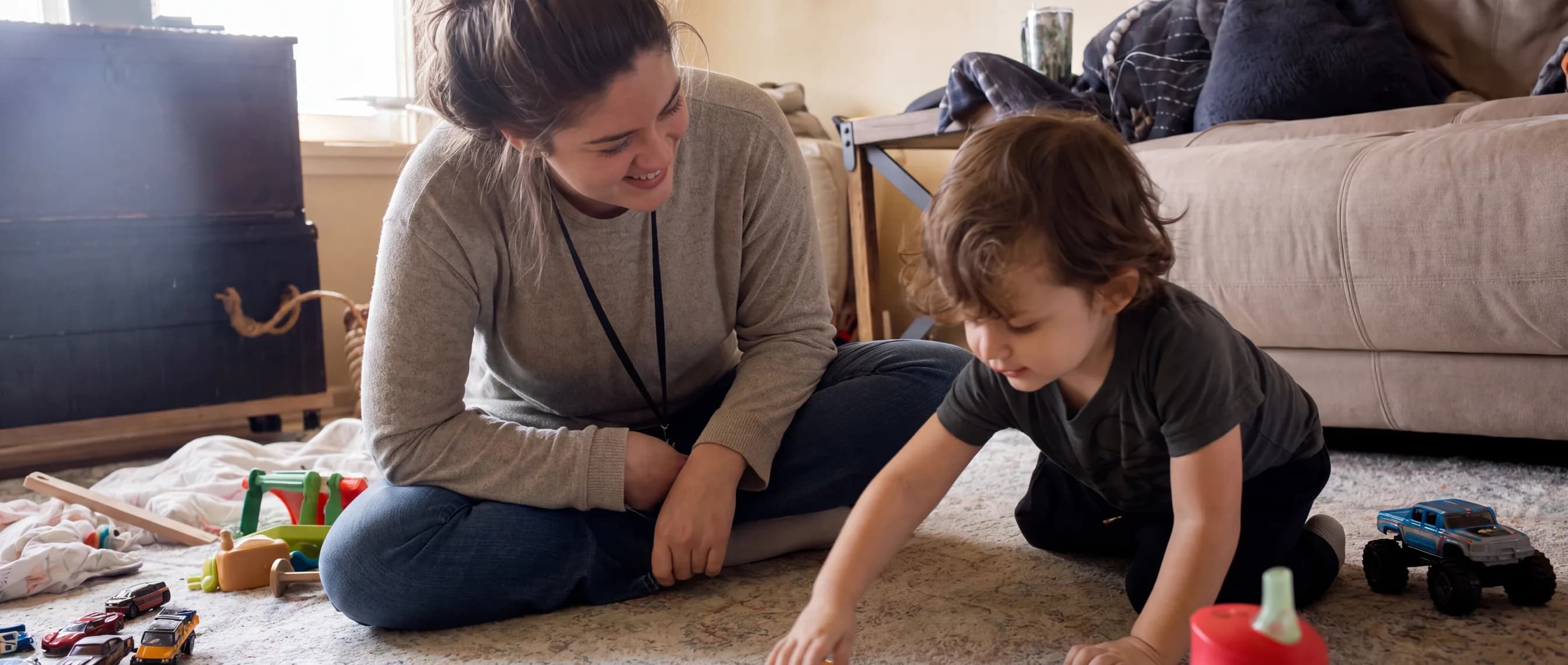 A child and behavior technician playing with toy cars on a living room rug during an in-home ABA session.